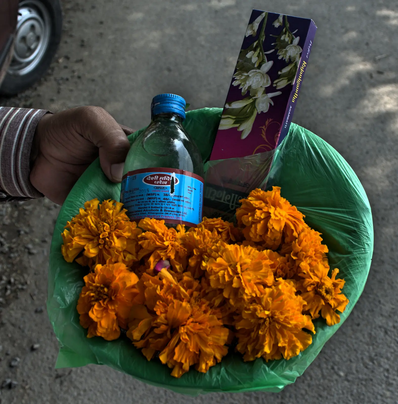 गेंदे के फूल, अगरबत्ती और मदिरा भोग की बोतल वाली पारंपरिक पूजन टोकरी